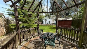 A wooden pergola with a table and chairs in a garden area.