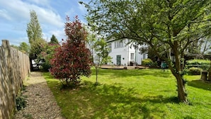 A well-maintained garden with a white house, a wooden fence, and a variety of trees and shrubs.
