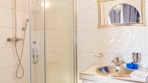 A bathroom with a glass-enclosed shower, a sink with a decorative basin, and a mirror with a gold frame. - Majorelle (Tours)