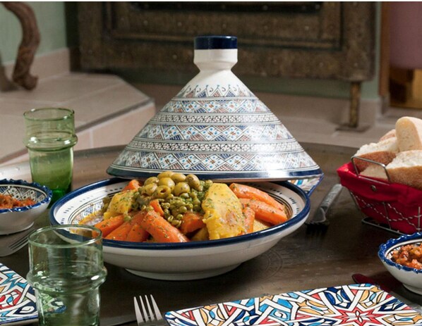 A traditional Moroccan tagine with vegetables, a couscous dish, and bread on a table.