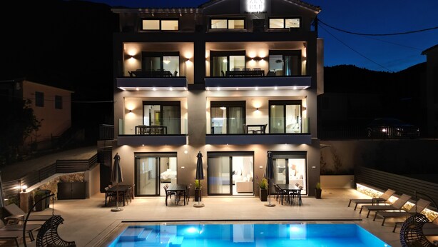 A modern two-story building with a swimming pool, outdoor seating, and a balcony with a dining area. - ZEN BLU Suites (Nikiana)