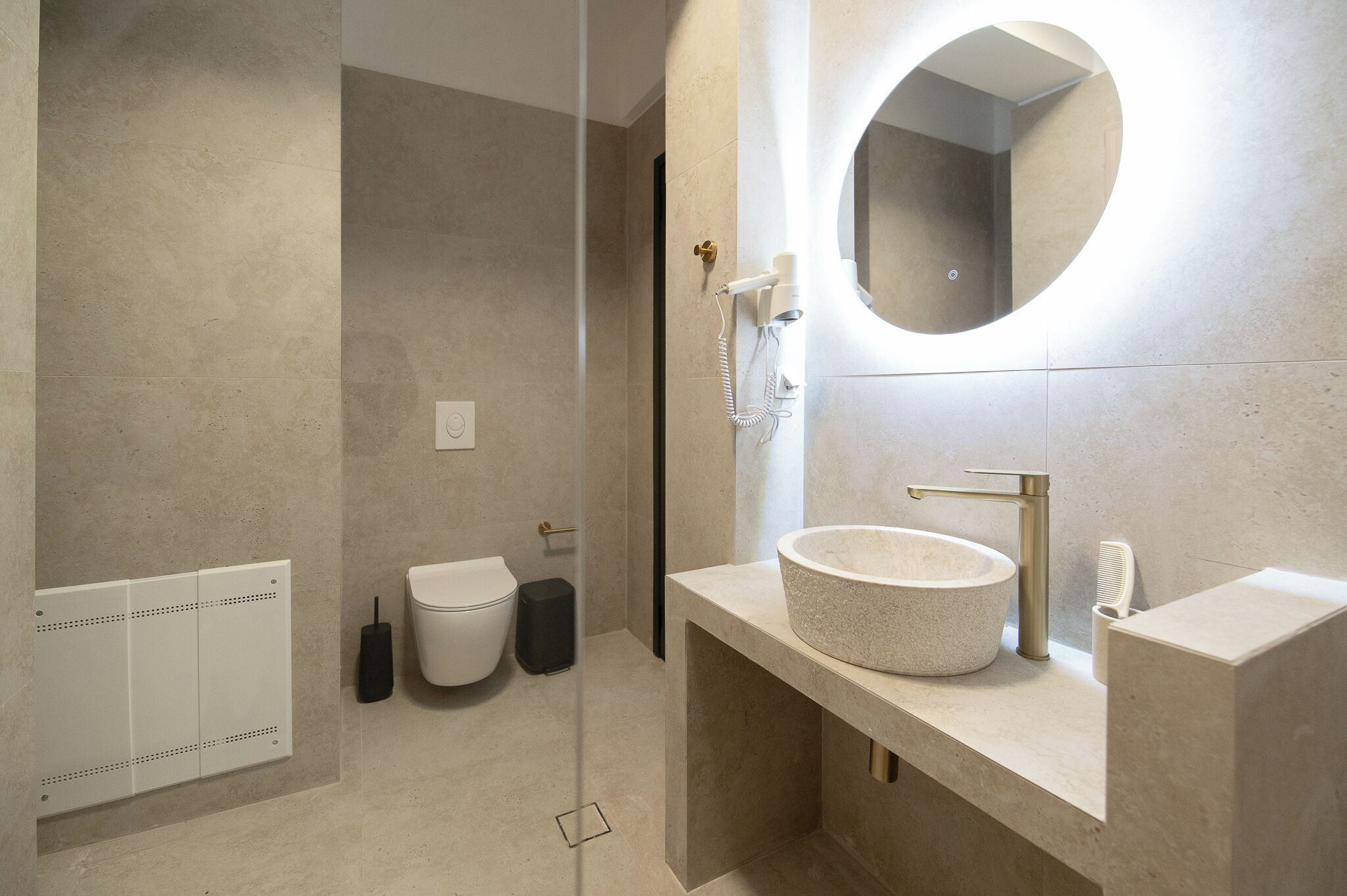 A modern bathroom with a round mirror, a pedestal sink, and a toilet.