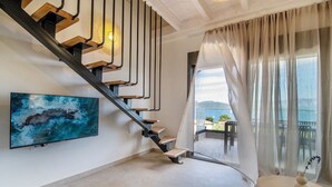 A modern interior with a staircase, a painting, a table with a vase, and a view through sheer curtains. - ZEN BLU Suites (Nikiana)