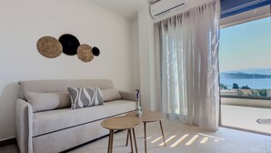 A modern living room with a sofa, two side tables, and a view of the sea through large windows. - ZEN BLU Suites (Nikiana)