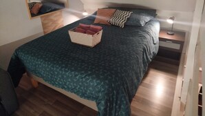 A bedroom with a bed, a nightstand with a lamp, a mirror, and a wooden headboard.