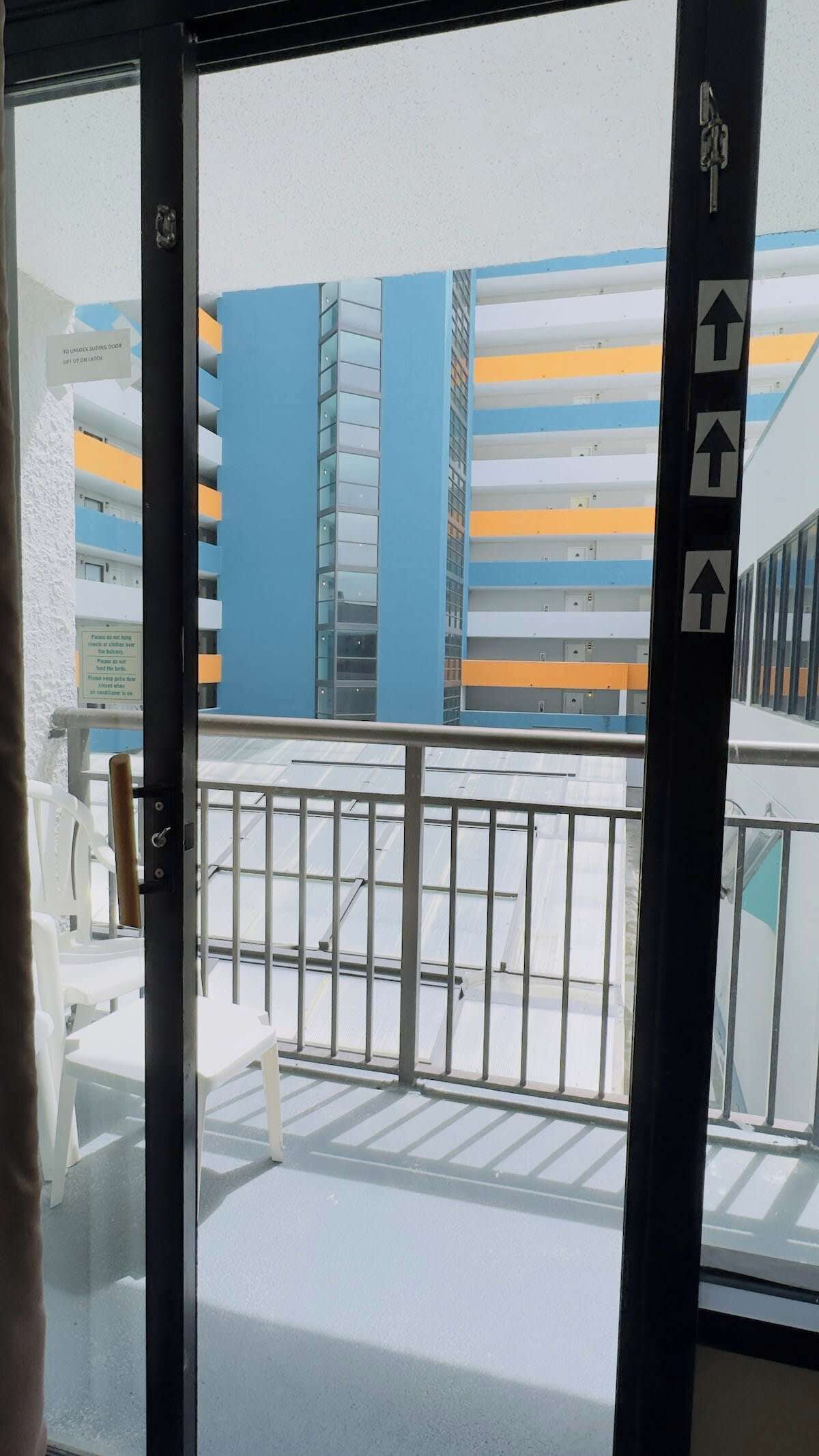 A view from a balcony with a metal railing, looking out at a multi-story building with blue and yellow stripes.