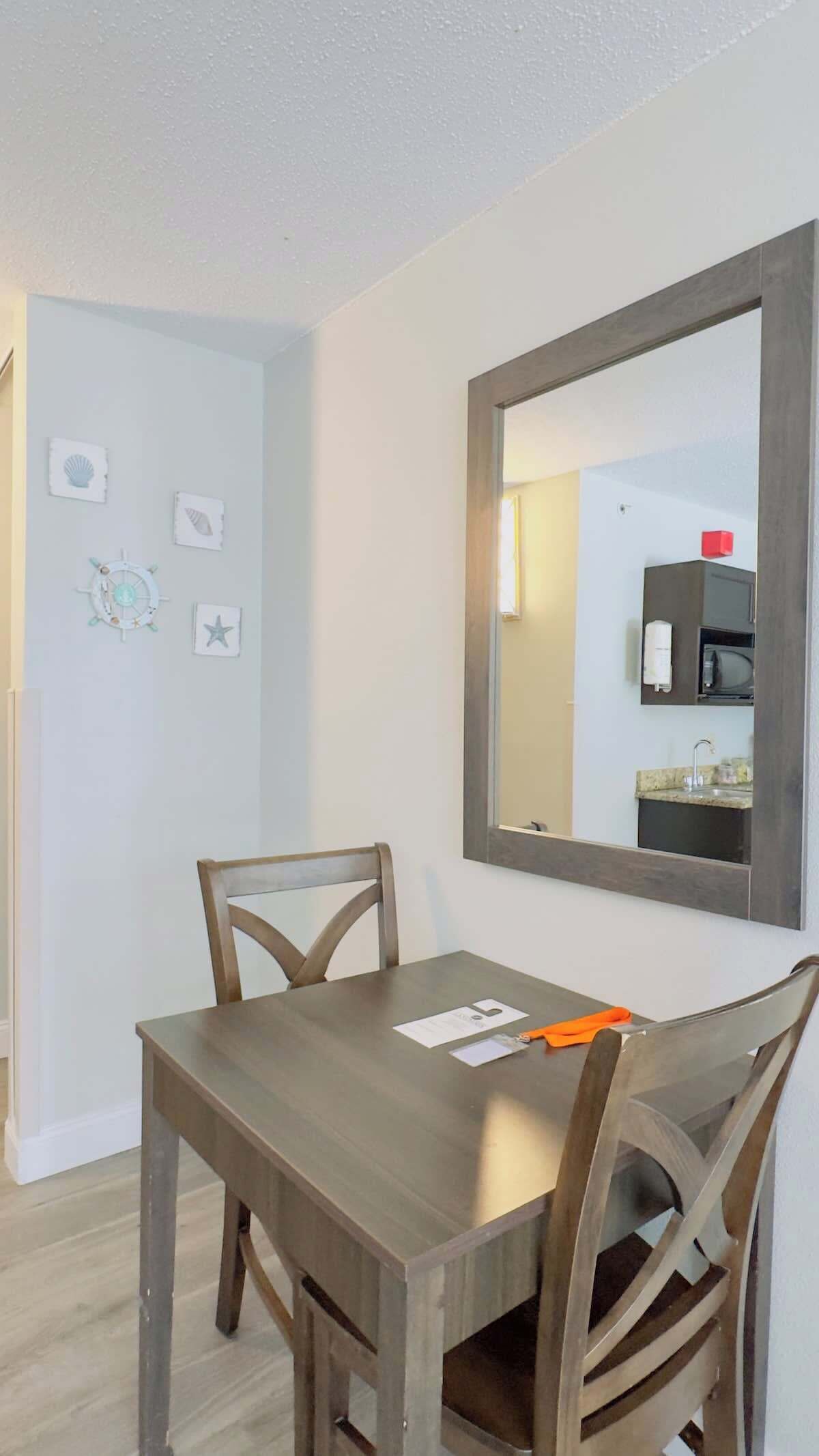 A dining area with a wooden table and chairs, a large mirror, and wall decorations including a ship wheel and star.
