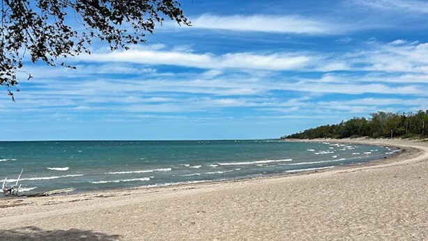 Une plage avec un rivage sablonneux et une mer calme, sous un ciel dégagé.