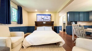 Une chambre avec un lit, deux chaises, un bureau, une télévision et un coin cuisine.