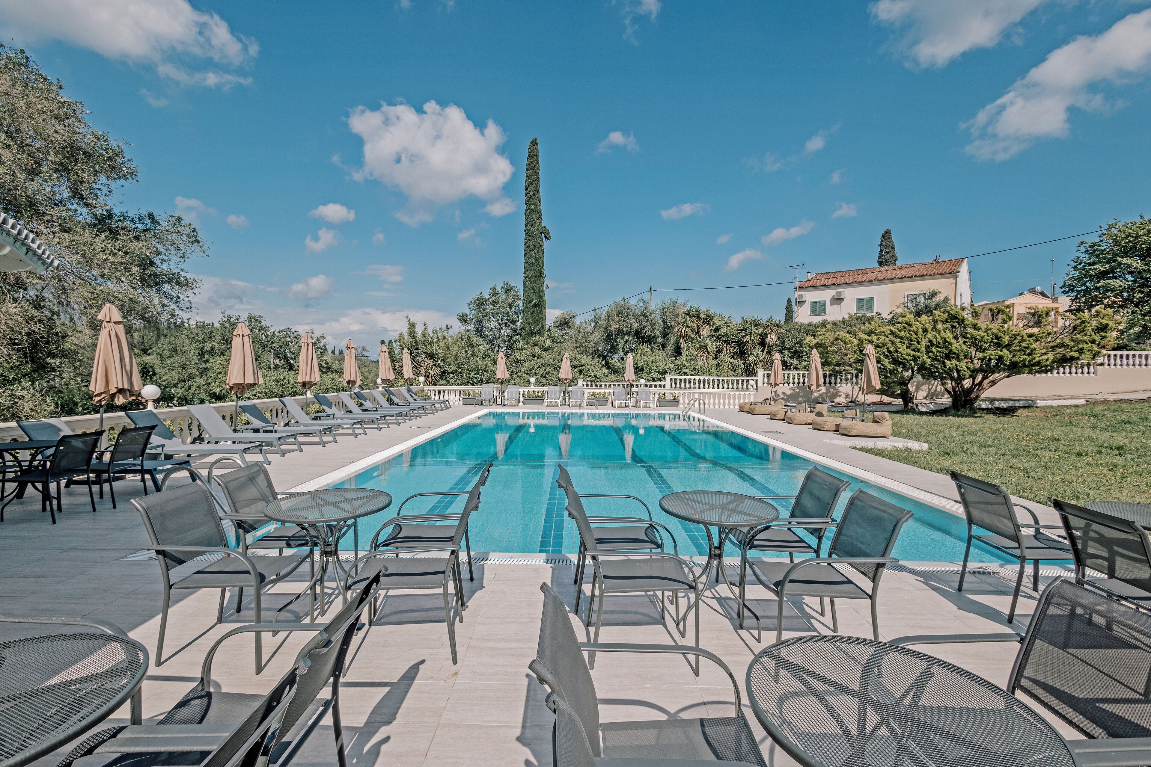 A swimming pool with lounge chairs and tables, surrounded by greenery and a tall tree.