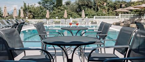 Un espace aménagé au bord de la piscine, avec des chaises longues et une table, entouré de parasols et de palmiers.