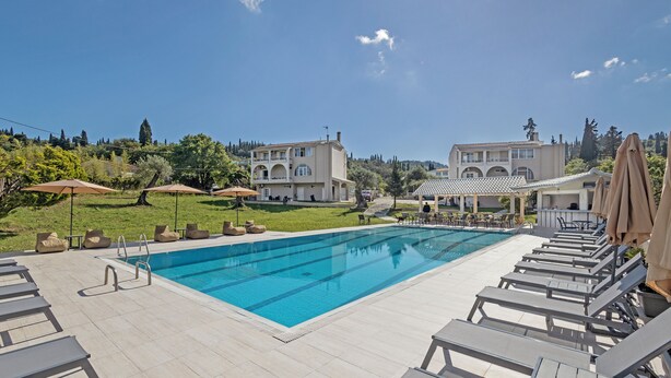 Piscina com espreguiçadeiras e guarda-sóis, cercada por edifícios e vegetação.