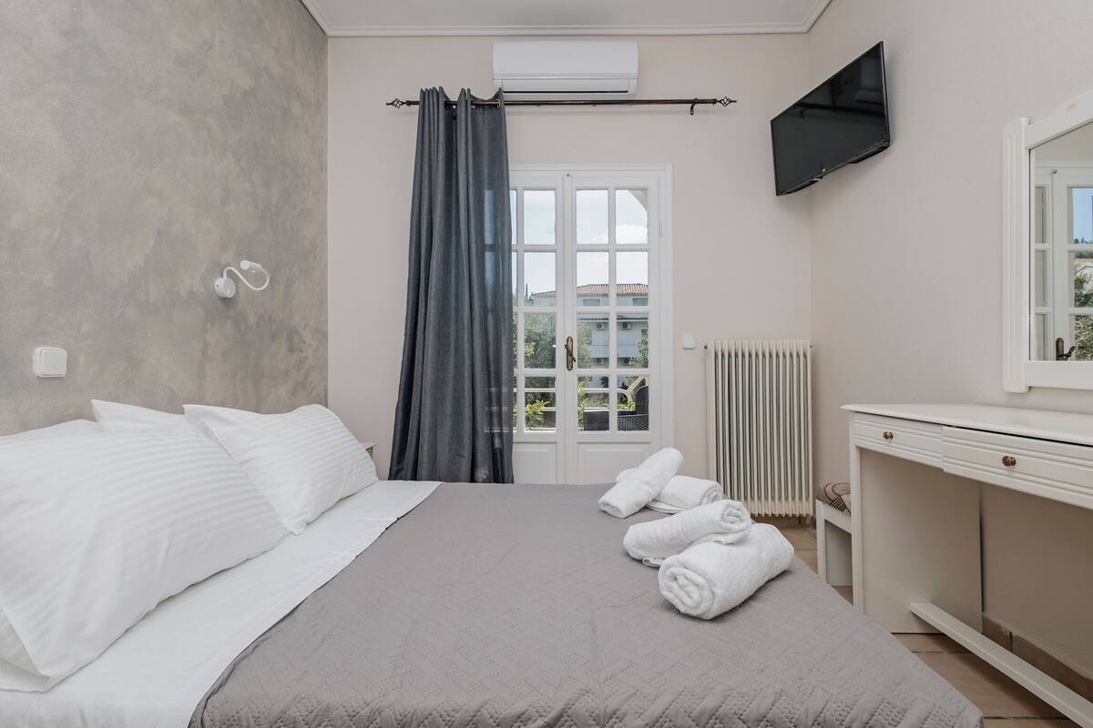 A bedroom with a bed, a TV, a window with curtains, a radiator, and a desk with drawers.