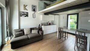 A modern apartment with a grey sofa, wooden flooring, a kitchen with white cabinets, and artwork on the walls. - Open-plan loft overlooking Lake Como with private parking space (Malgrate)
