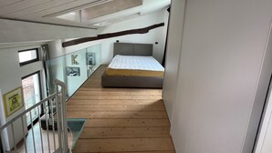 A narrow, wooden-floored corridor leading to a bedroom with a bed and a large window. - Open-plan loft overlooking Lake Como with private parking space (Malgrate)