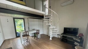 A modern apartment with a dining area, a TV, and a spiral staircase. - Open-plan loft overlooking Lake Como with private parking space (Malgrate)