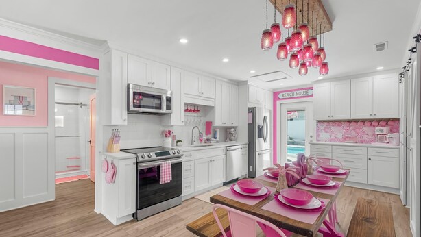 Une cuisine moderne avec des meubles blancs, des touches de rose et une table à manger en bois, agrémentée d’une vaisselle rose.