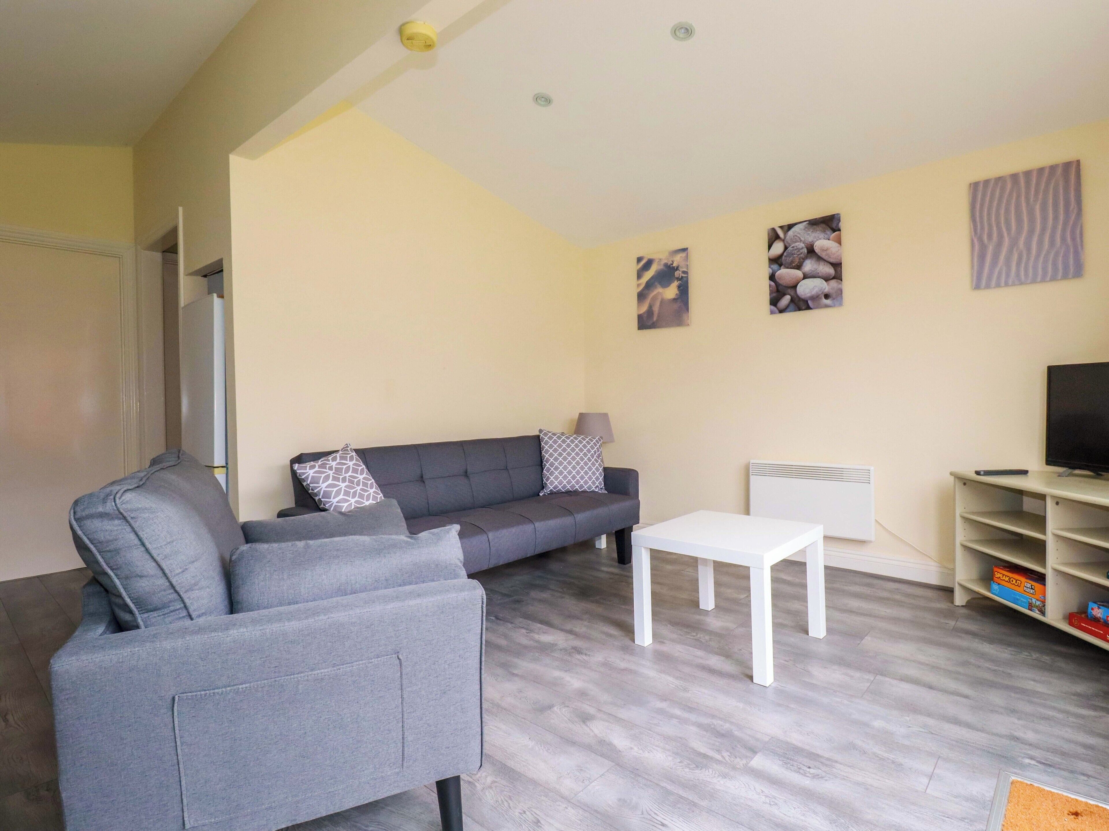 A living room with a grey sofa, a white coffee table, and a TV stand with a remote.