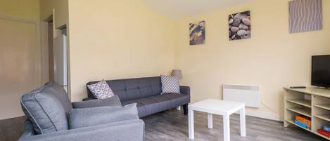 A living room with a grey sofa, a white coffee table, and a TV stand with a remote.