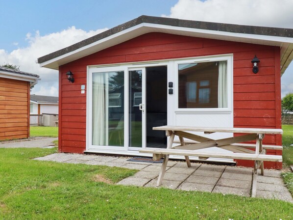 A red building with a white door and windows, a picnic table in front, and a grassy yard.