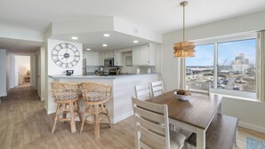 Una cocina moderna con armarios blancos, un reloj grande y un comedor con mesa de madera y sillas de mimbre.