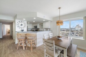 Een moderne keuken met witte kastjes, een grote klok, en een eethoek met een houten tafel en rieten stoelen.