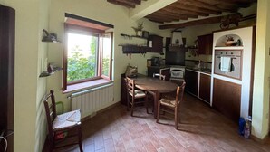Eine rustikale Küche mit Holztisch und -stühlen, einem Fenster mit Blick auf Grünflächen und einem eingebauten Backofen.