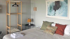 Ett sovrum med en säng, en trästege, en lampa, en luftkonditioneringsanläggning och en målning av en fyr.