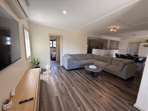 A modern living room with a sectional sofa, a coffee table, and a flat-screen TV mounted on the wall. - Shore Beats Work - Large entertaining area! Dog friendly! (Stansbury)