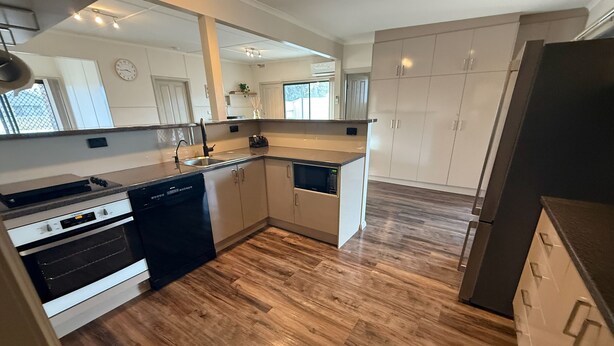 A modern kitchen with wooden flooring, built-in appliances, and white cabinetry.