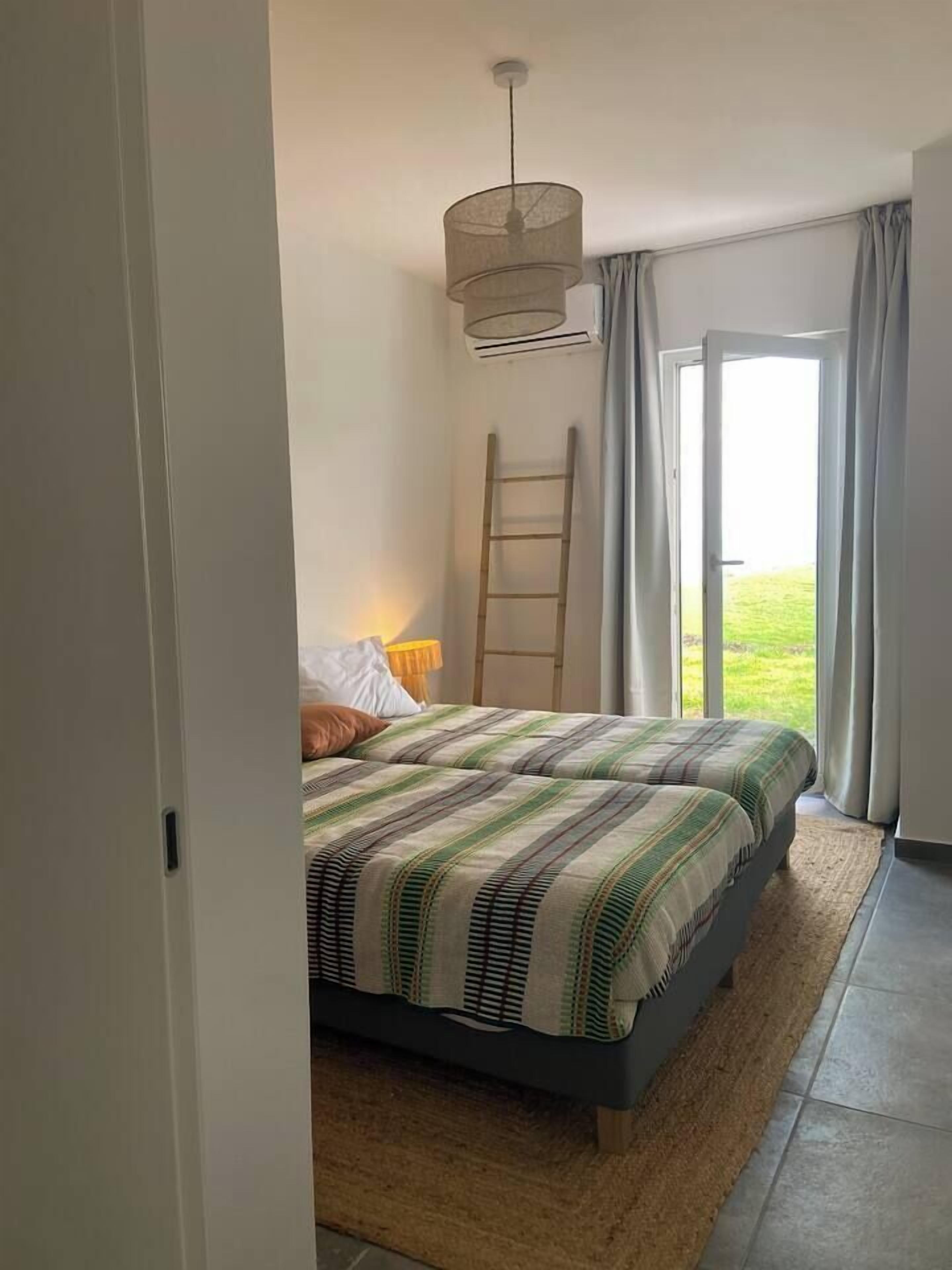 Ein Schlafzimmer mit Bett, einer Leiter, einem Fenster und Blick ins Freie.
