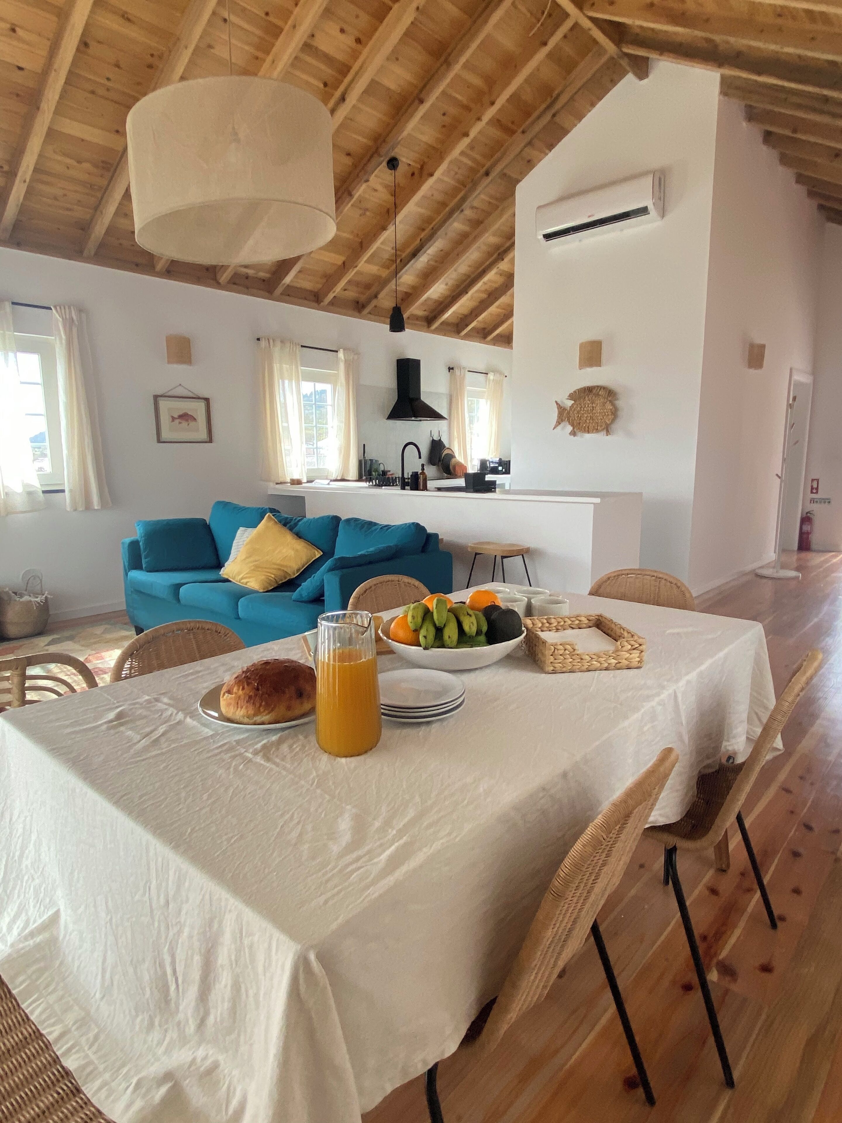 A dining area with a table set for breakfast, a blue sofa in the background, and a kitchen visible through an open door.