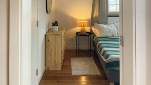 Une chambre à coucher avec un lit, une table de chevet avec une lampe, une petite armoire et une fenêtre avec des rideaux.