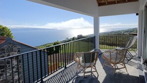 Un balcon avec deux fauteuils en osier, un mur de pierre et une vue sur la mer.