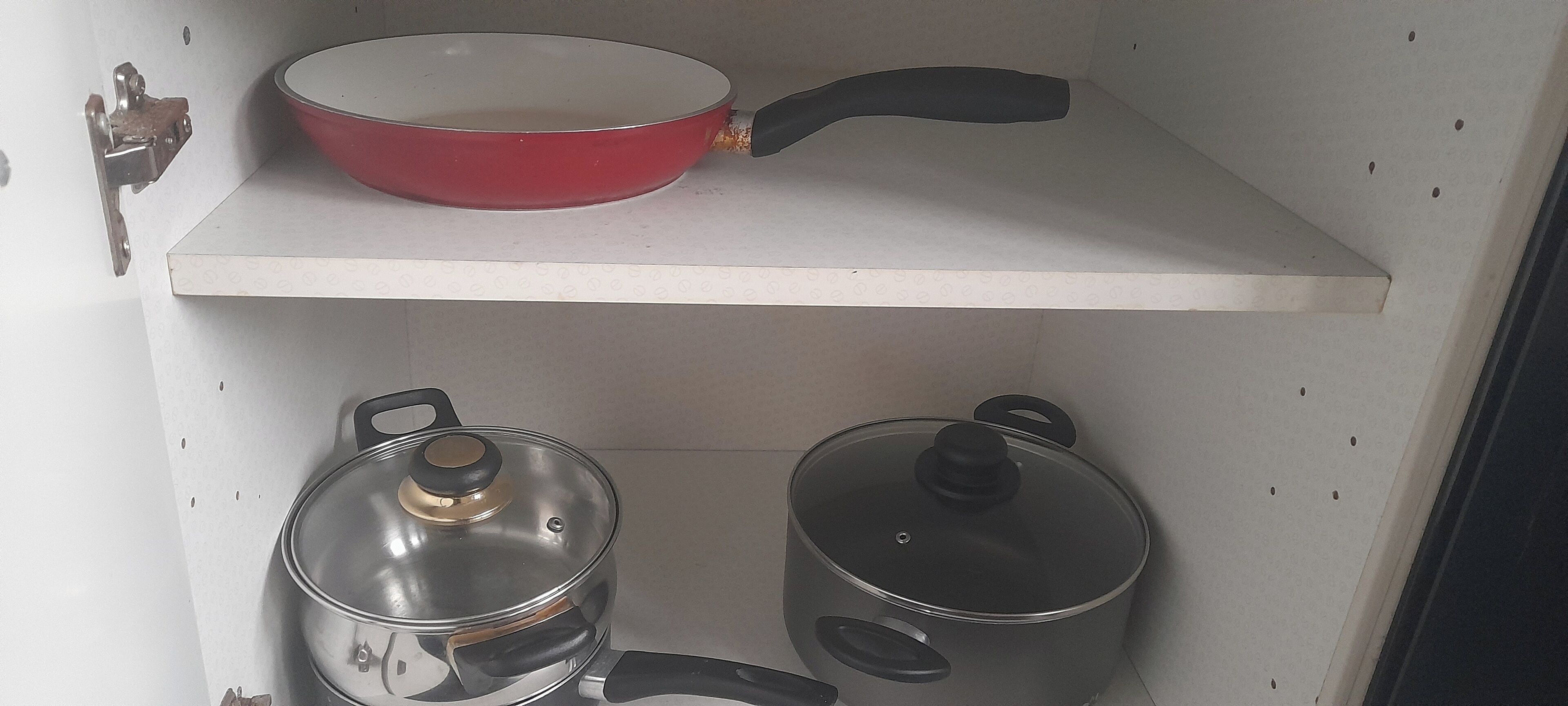 A kitchen shelf with a red frying pan, a stainless steel pot with a lid, and a pot with a lid.