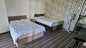 Habitación de hotel con dos camas, alfombra a rayas, pared con estampado de árbol y un ventilador de pie.