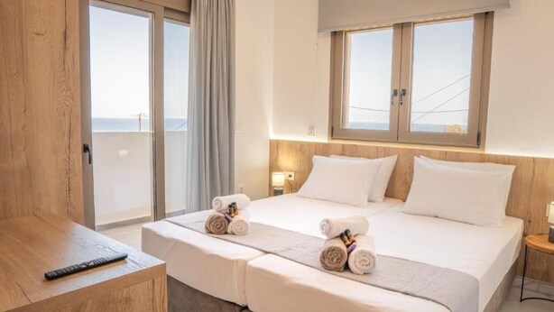 A hotel room with a bed, a desk, and a view of the sea. - Villa Leandros Premium Suites (Agia Varvara)