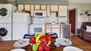A compact kitchen with a washing machine, microwave, and oven. There is a dining area with a fruit basket and plates. - Pool, secluded but mins to strip NO stairs Fishing (Branson)