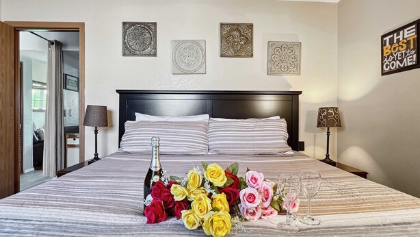 A neatly made bed with a bottle of champagne, a bouquet of flowers, and glasses on the bed. - Pool, secluded but mins to strip NO stairs Fishing (Branson)