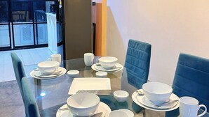 En matplats med ett glasbord för fyra personer, blå vadderade stolar och ett svart kylskåp i bakgrunden.