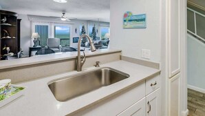A kitchen with a stainless steel sink, white cabinetry, and a view of a living room with a Christmas tree. - Bayfront Kontiki 107 (Rockport)