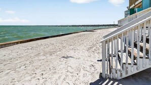 A beach with a wooden staircase leading to a building with balconies. - Bayfront Kontiki 107 (Rockport)