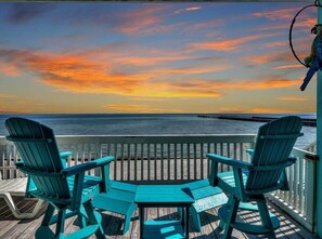A wooden deck with two chairs and a table, overlooking a body of water and a pier. - Bayfront Kontiki 107 (Rockport)