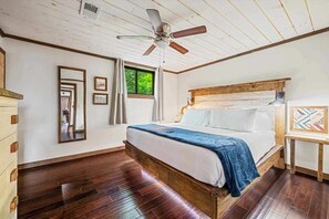Un dormitorio con cama de madera, ventilador de techo y una ventana grande.