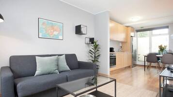 A modern living room with a grey sofa, a glass coffee table, and a kitchen in the background.
