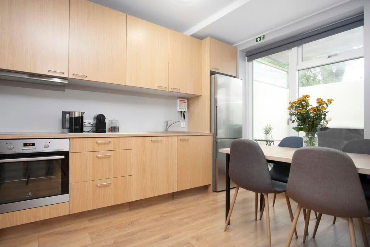 A modern kitchen with wooden cabinets, a stainless steel refrigerator, and a dining area with two chairs and a table.