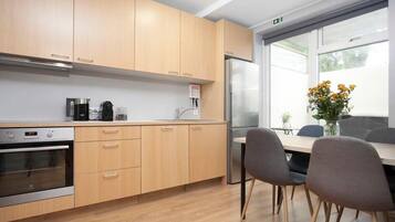 A modern kitchen with wooden cabinets, a stainless steel refrigerator, and a dining area with two chairs and a table.