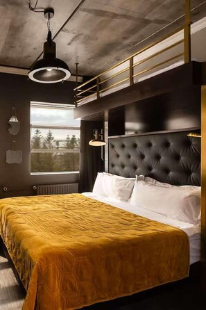 A modern bedroom with a large bed, a black tufted headboard, and a window with a view of trees. - Urban Reykjavik Triple studio with bunk bed (Reykjavík)