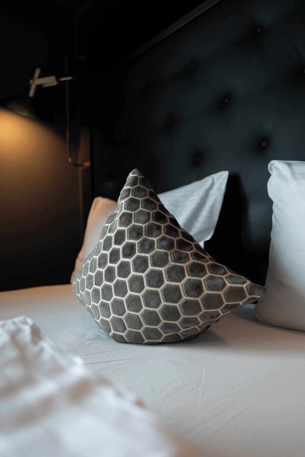 Una cama con cabecera oscura, almohadas blancas y un cojín estampado.