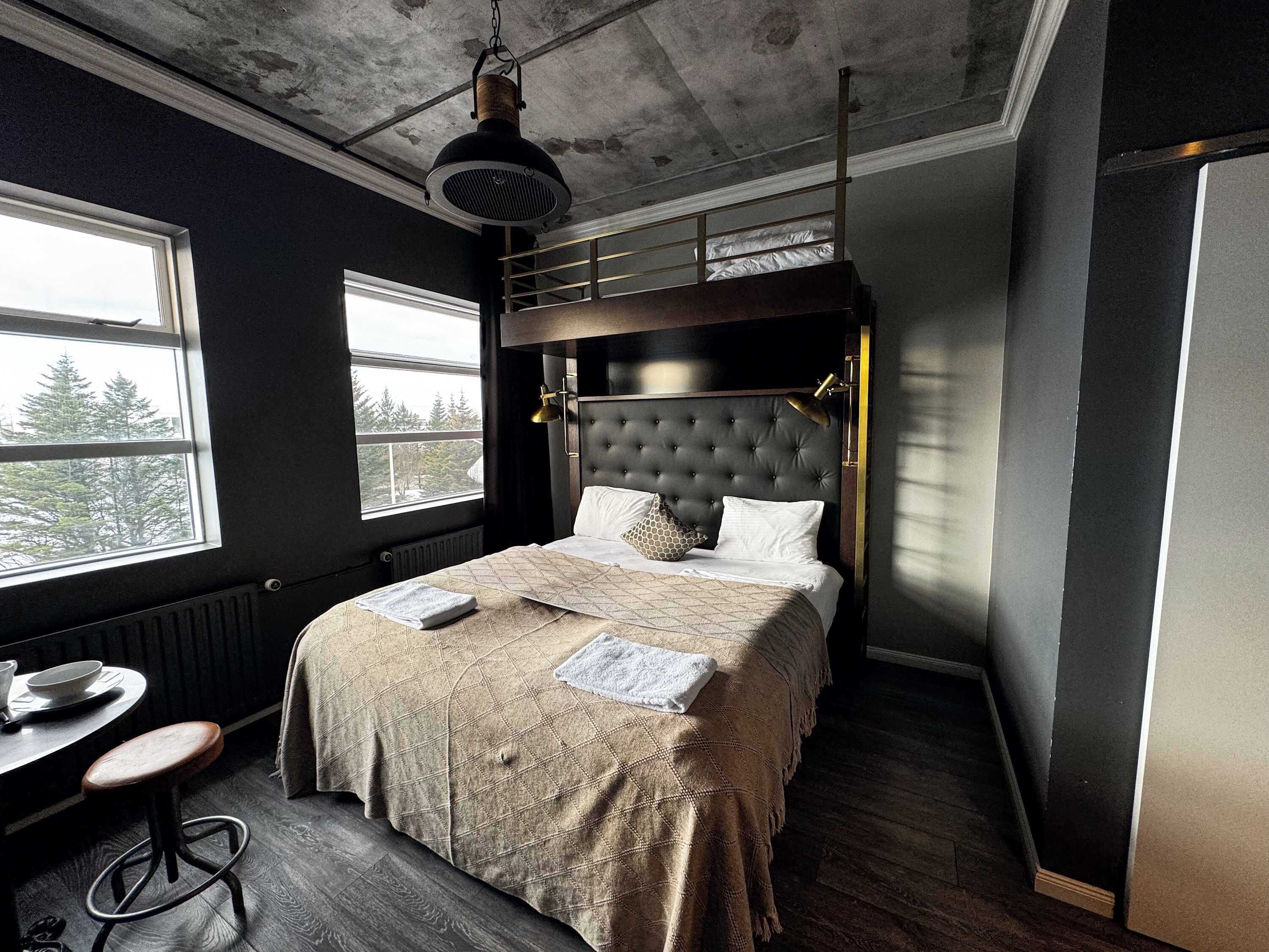 A bedroom with a bunk bed, a desk with a chair, and a large window.